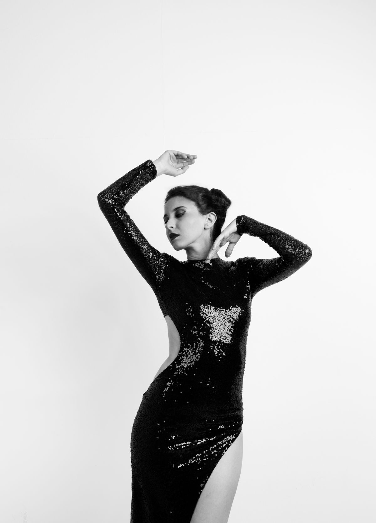 A woman in a black dress with arms raised — sculptural drama