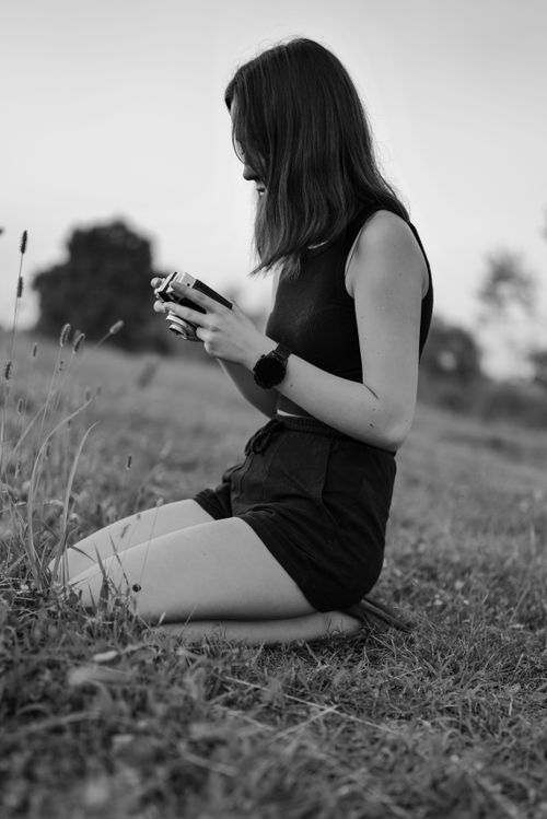 Free Black and white photo of a woman kneeling in a field holding a camera. Stock Photo
