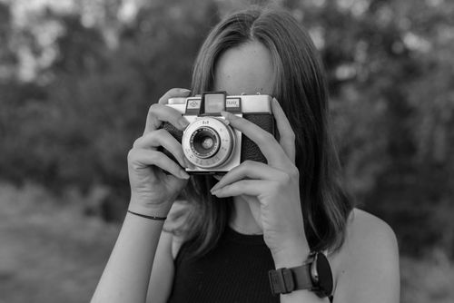Free Black and white portrait of a woman capturing a moment with a vintage camera outdoors. Stock Photo