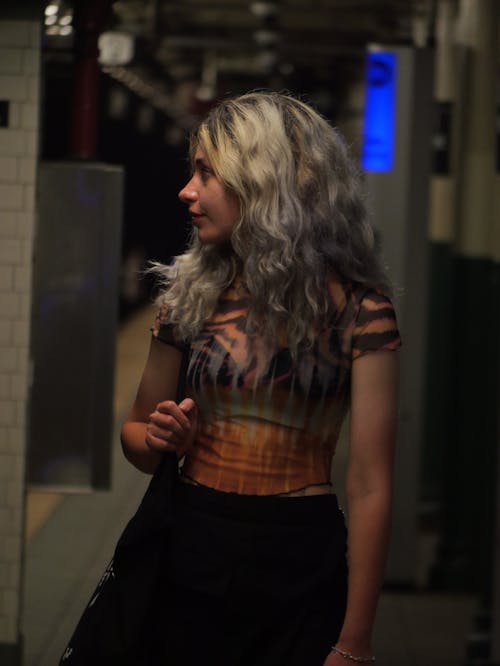 A woman with long hair and a black top walks down a subway platform