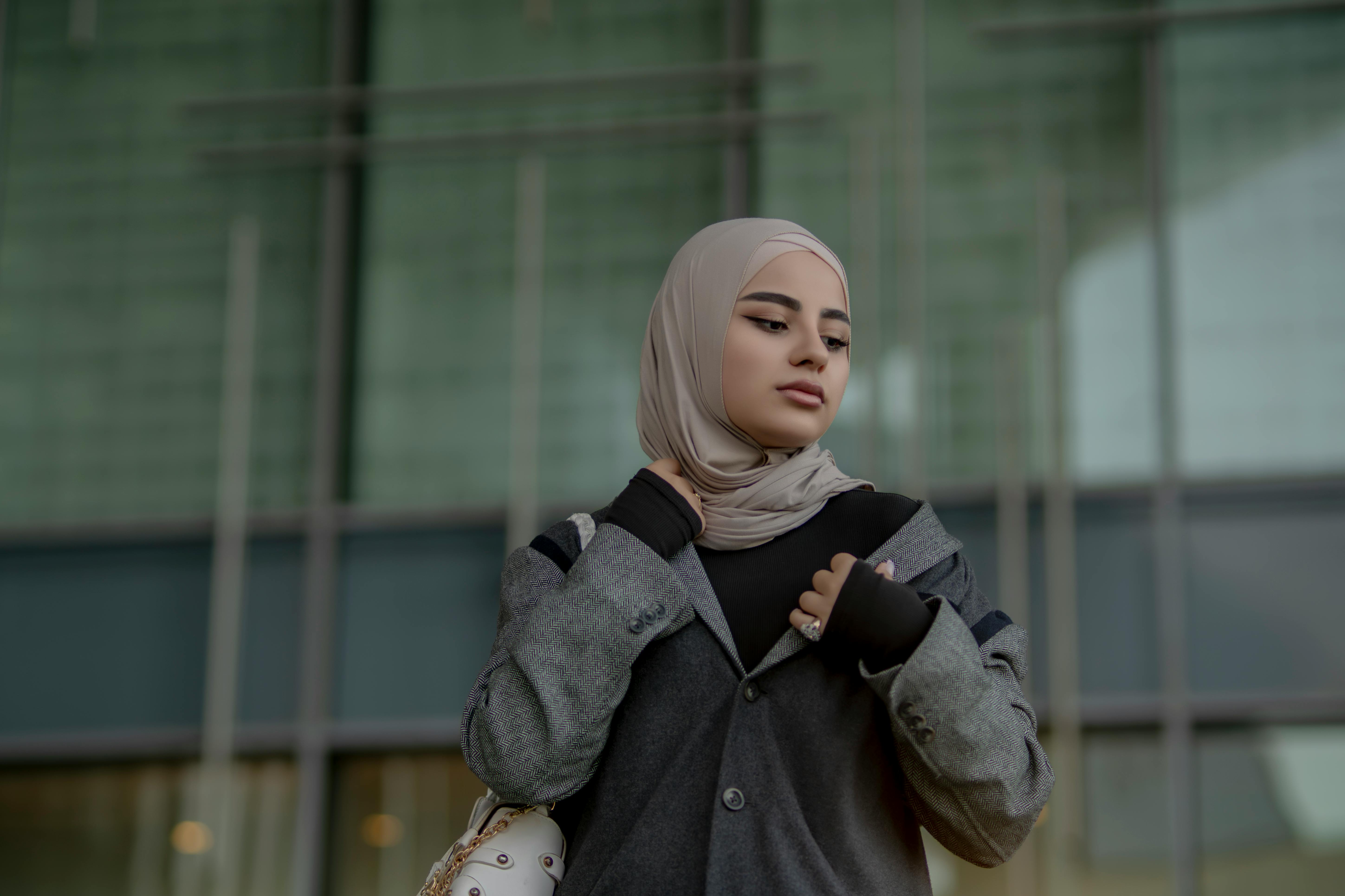 Elegantly dressed woman wearing a hijab standing outside modern architecture.