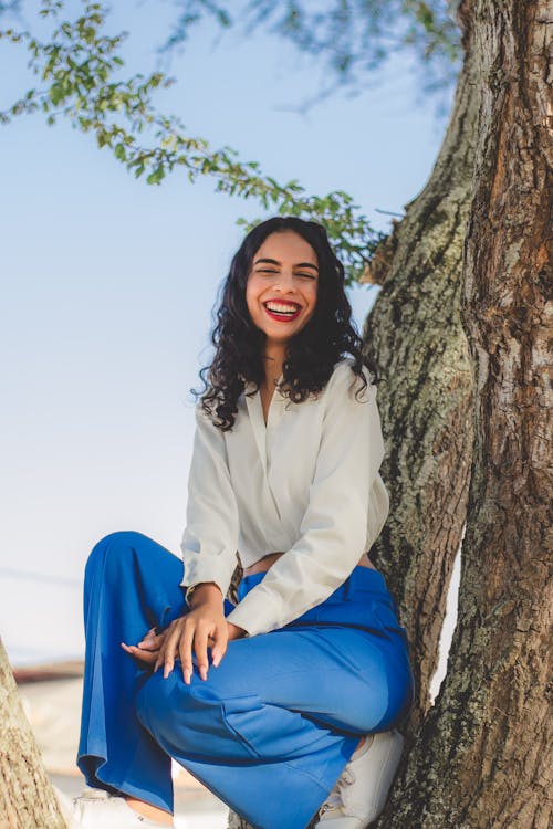 Laughing Woman in Blue Pants Sitting on Tree