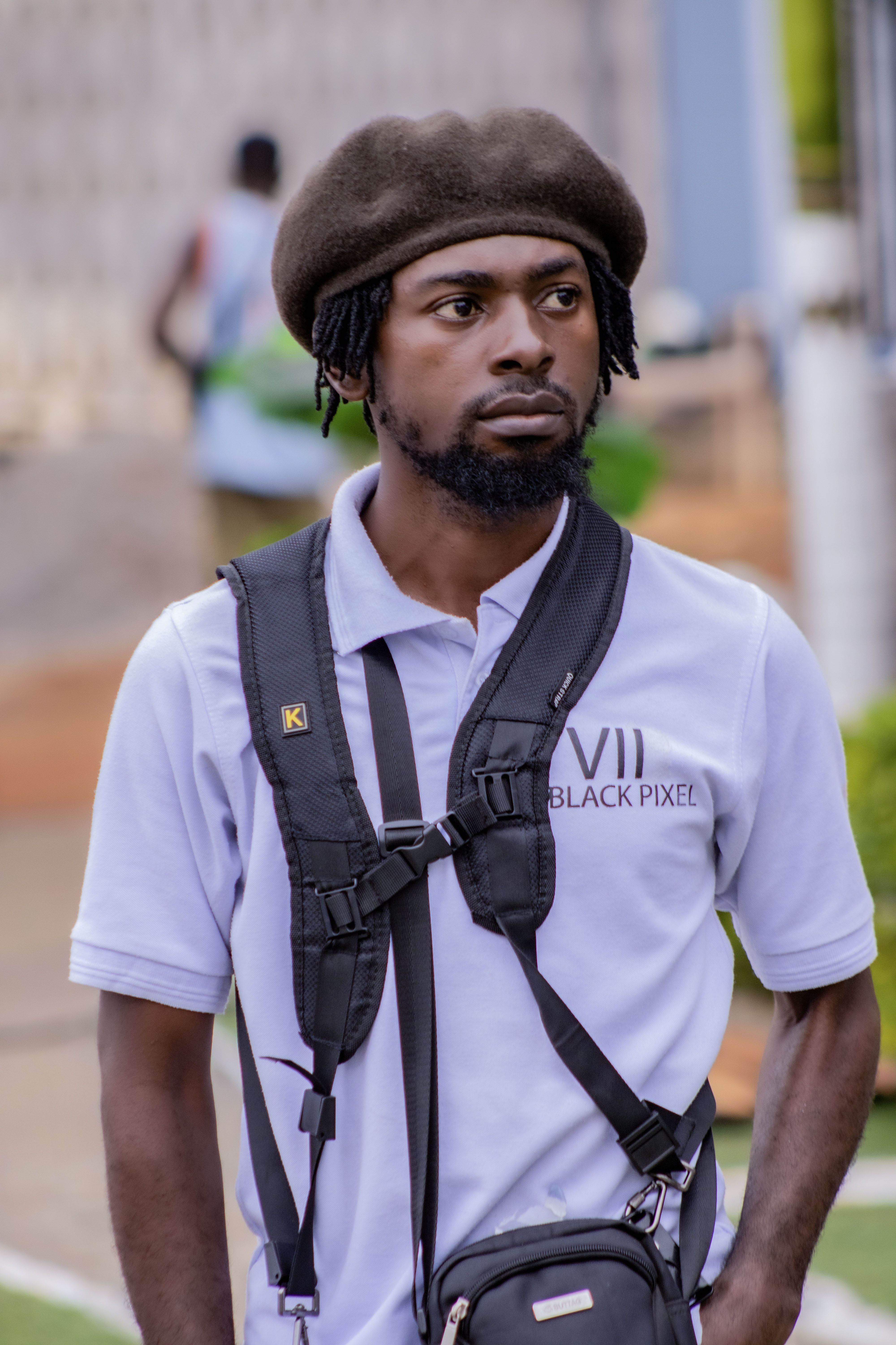 A fashionable man with a cap and beard walking outdoors in casual attire, exuding confidence.