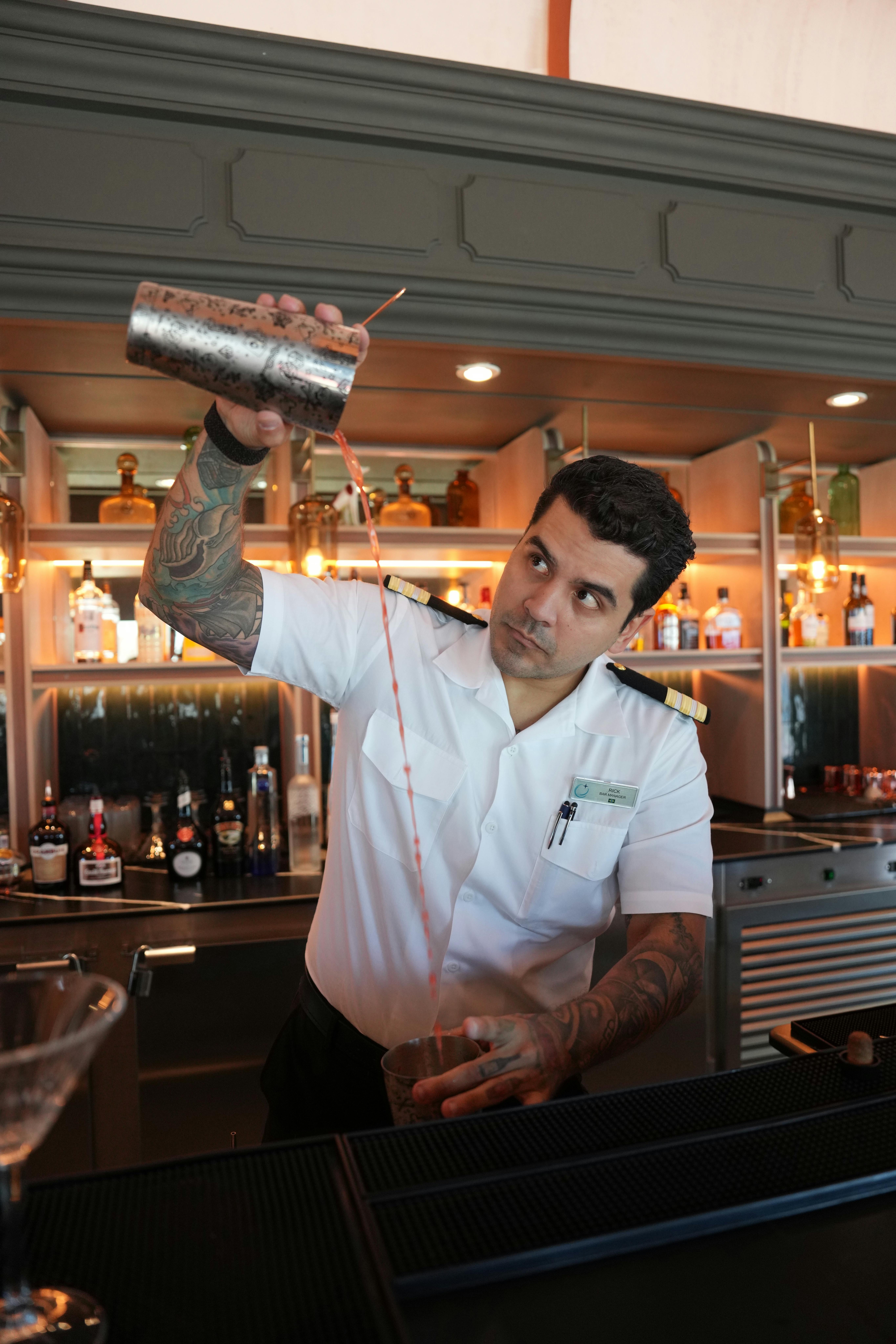 A professional bartender expertly pours a cocktail at a modern bar counter.