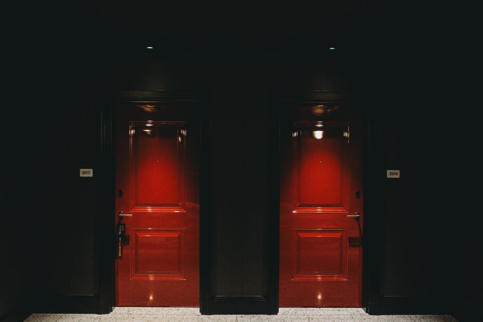 Moody image of two illuminated red doors in a dark hotel hallway, creating a mysterious ambiance.