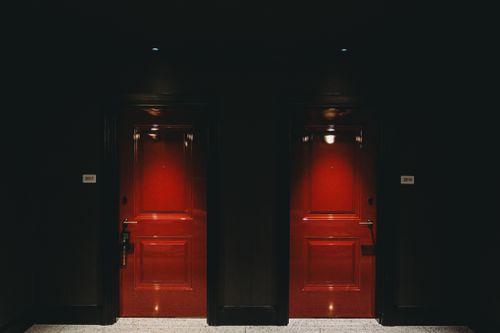 Free Moody image of two illuminated red doors in a dark hotel hallway, creating a mysterious ambiance. Stock Photo