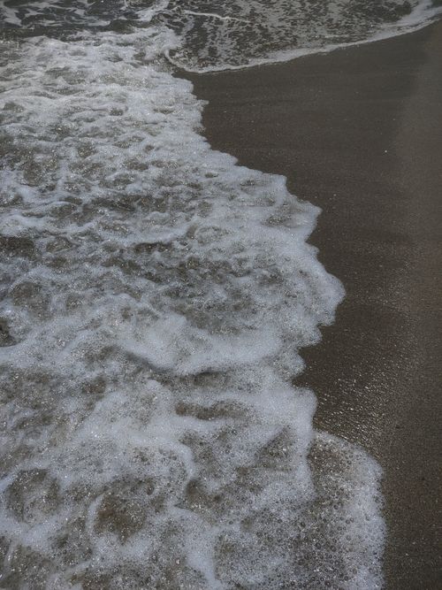 Free Close-up view of gentle ocean waves lapping on a sandy beach under a clear sky. Stock Photo