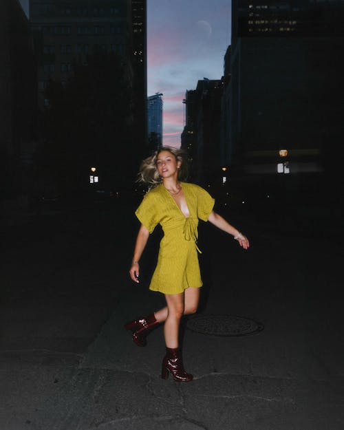 Young Woman in a Dress and Heels Standing on a Street in City at Dusk 