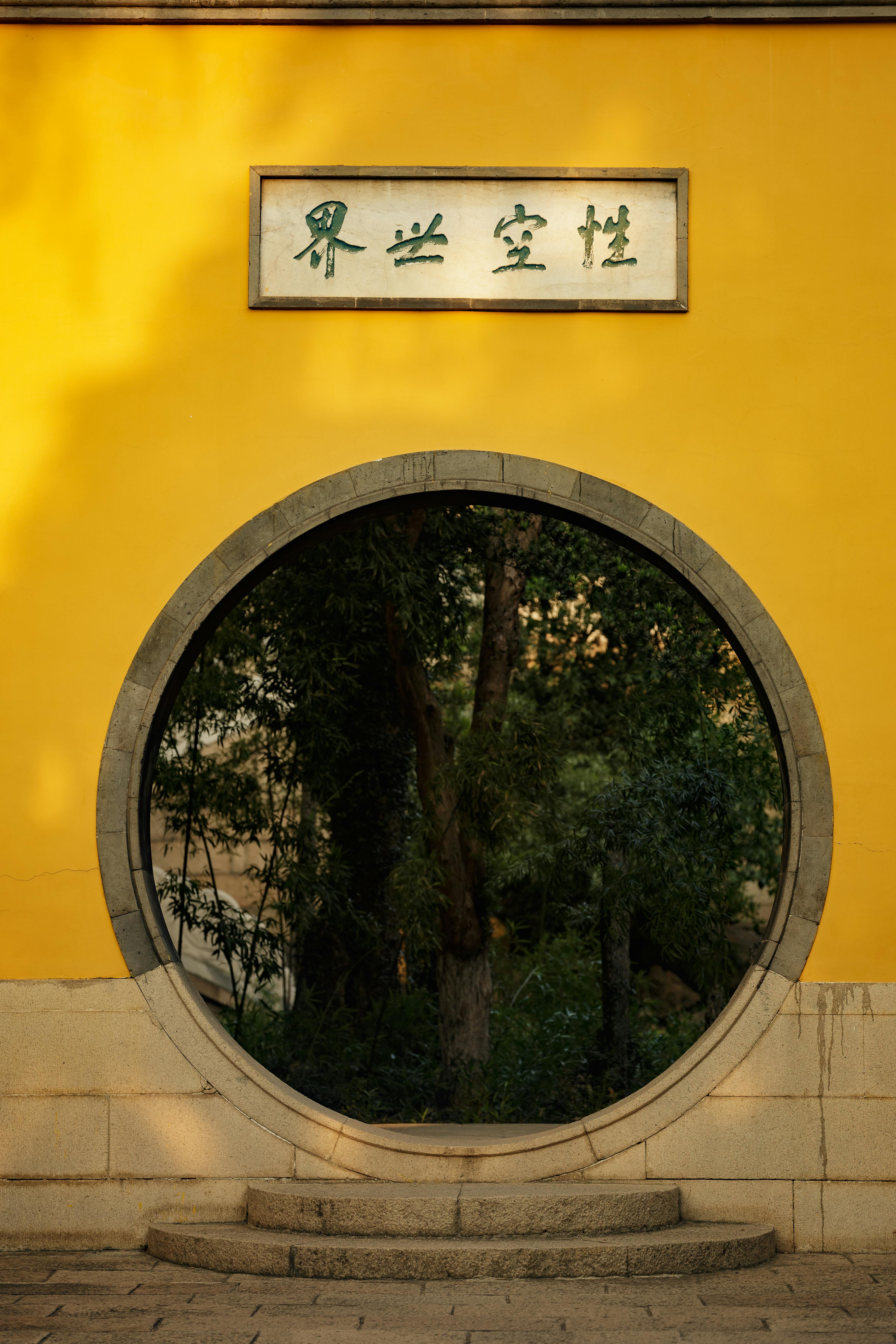 Yellow wall with a unique circular entrance and forest view, embodying traditional Asian design.