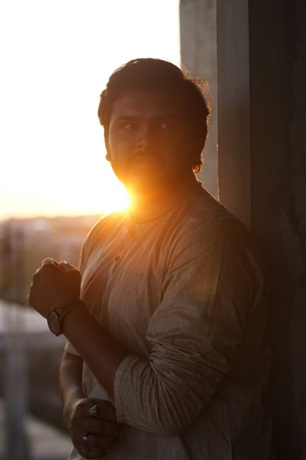 Silhouette of a man with a mustache posing at sunset, wearing rings and a watch.