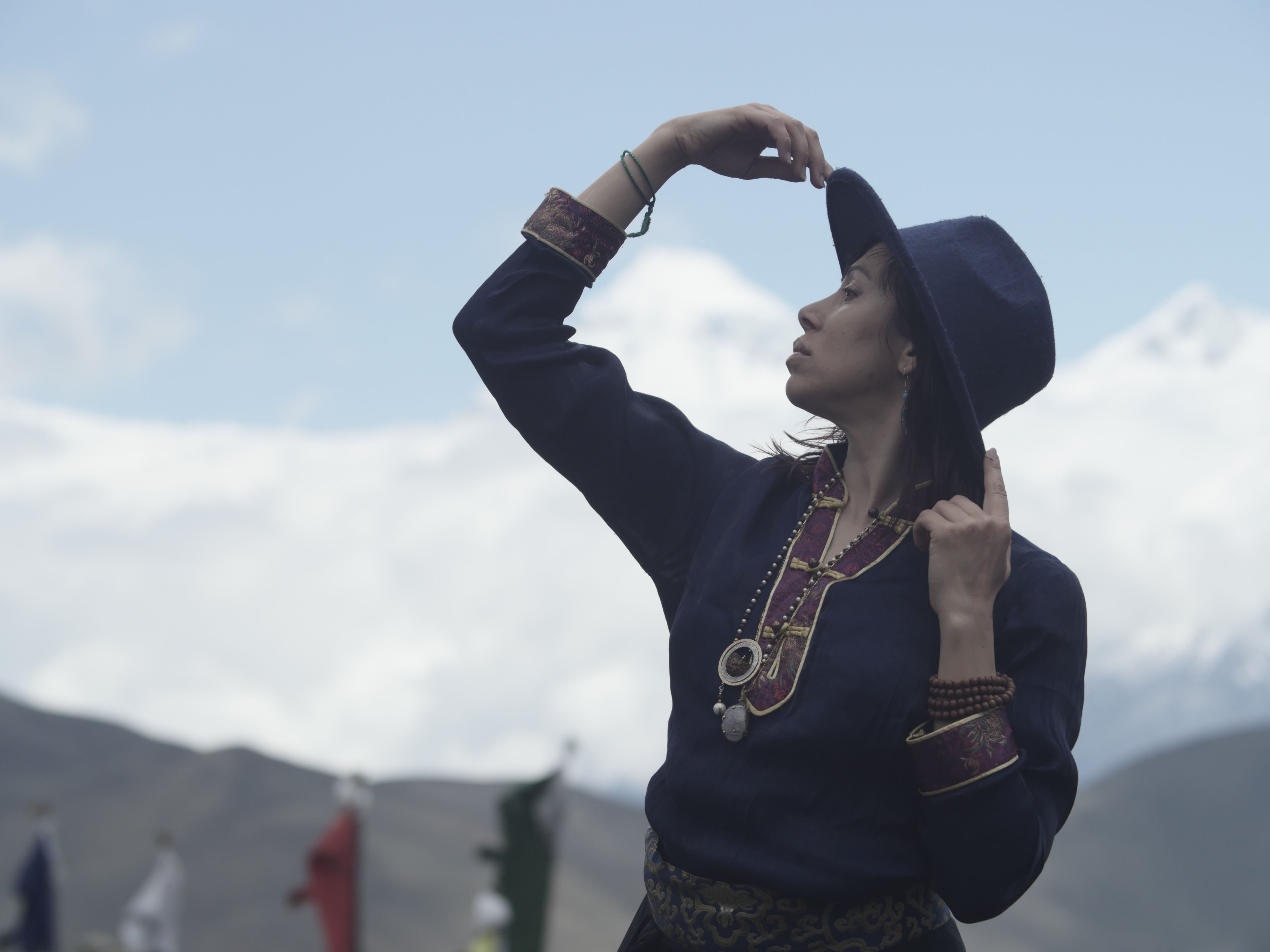 A woman in traditional attire poses elegantly against a mountain landscape.