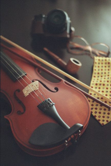A vintage violin with a bow, camera, and accessories on a dark table. Perfect for music and nostalgia themes.