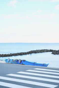 A scenic view of a blue boat by the sea, with a pedestrian crossing in the foreground.
