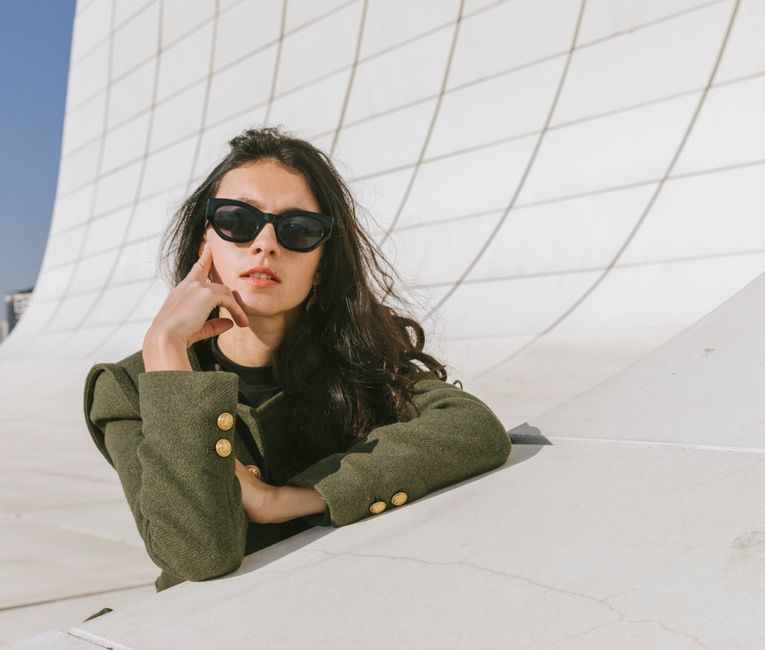 Young woman in sunglasses poses against modern architecture in Baku, Azerbaijan.