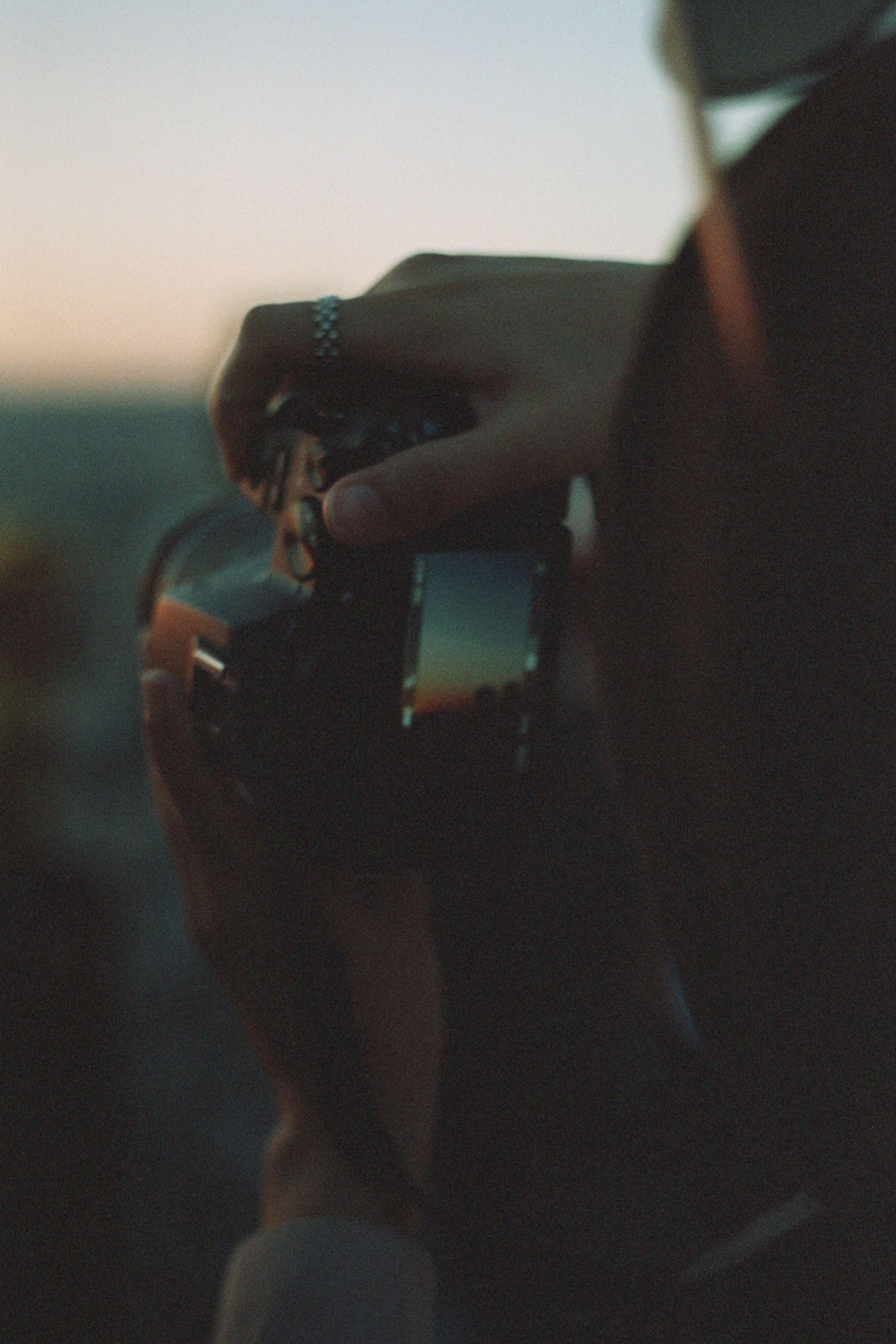 Close-up of a person holding a camera, capturing an evening scene.