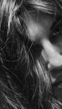 A mysterious black and white close-up portrait of a woman with tousled hair obscuring her face.
