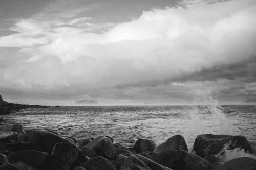 Free A dramatic black and white seascape with crashing waves against rocky shoreline under a cloudy sky. Stock Photo