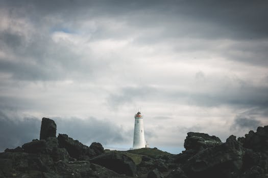 A striking lighthouse stands on the rocky Icelandic coast under a stormy sky.