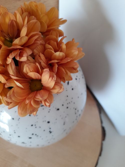 Free Close-up of vibrant orange flowers arranged in a stylish speckled vase indoors. Stock Photo