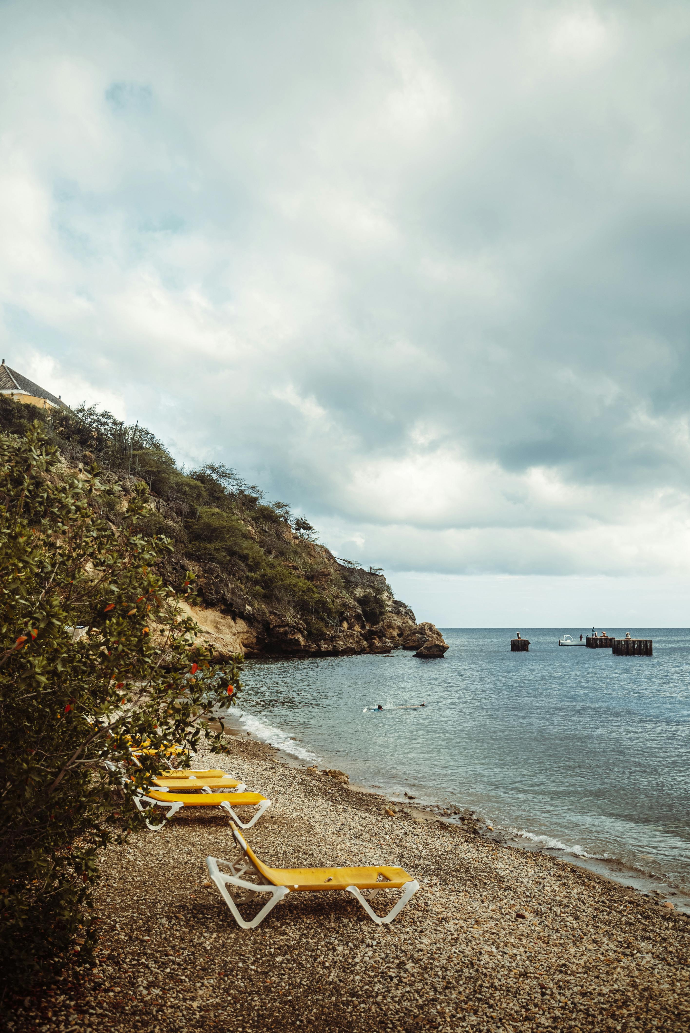 A tranquil beach in Curacao featuring deckchairs, rocky coastline, and a moody sky.