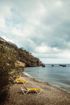 A tranquil beach in Curacao featuring deckchairs, rocky coastline, and a moody sky.