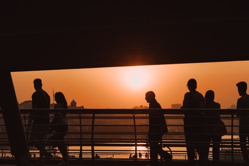 Free Silhouetted people crossing a footbridge at sunset, creating an urban scene bathed in warm golden hues. Stock Photo