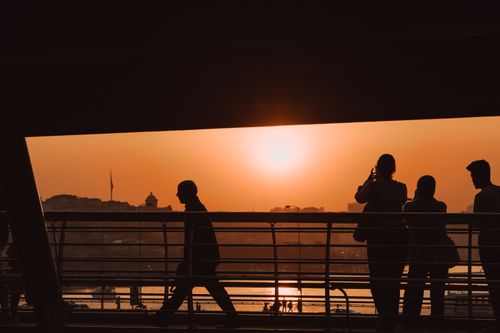 Free Silhouetted pedestrians on a footbridge during sunset, with a cityscape backdrop. Stock Photo