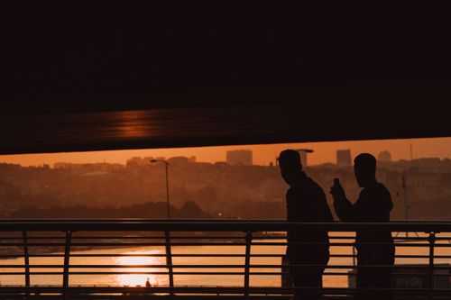 Free Silhouettes of people walking on a footbridge during a vibrant sunset in an urban setting. Stock Photo