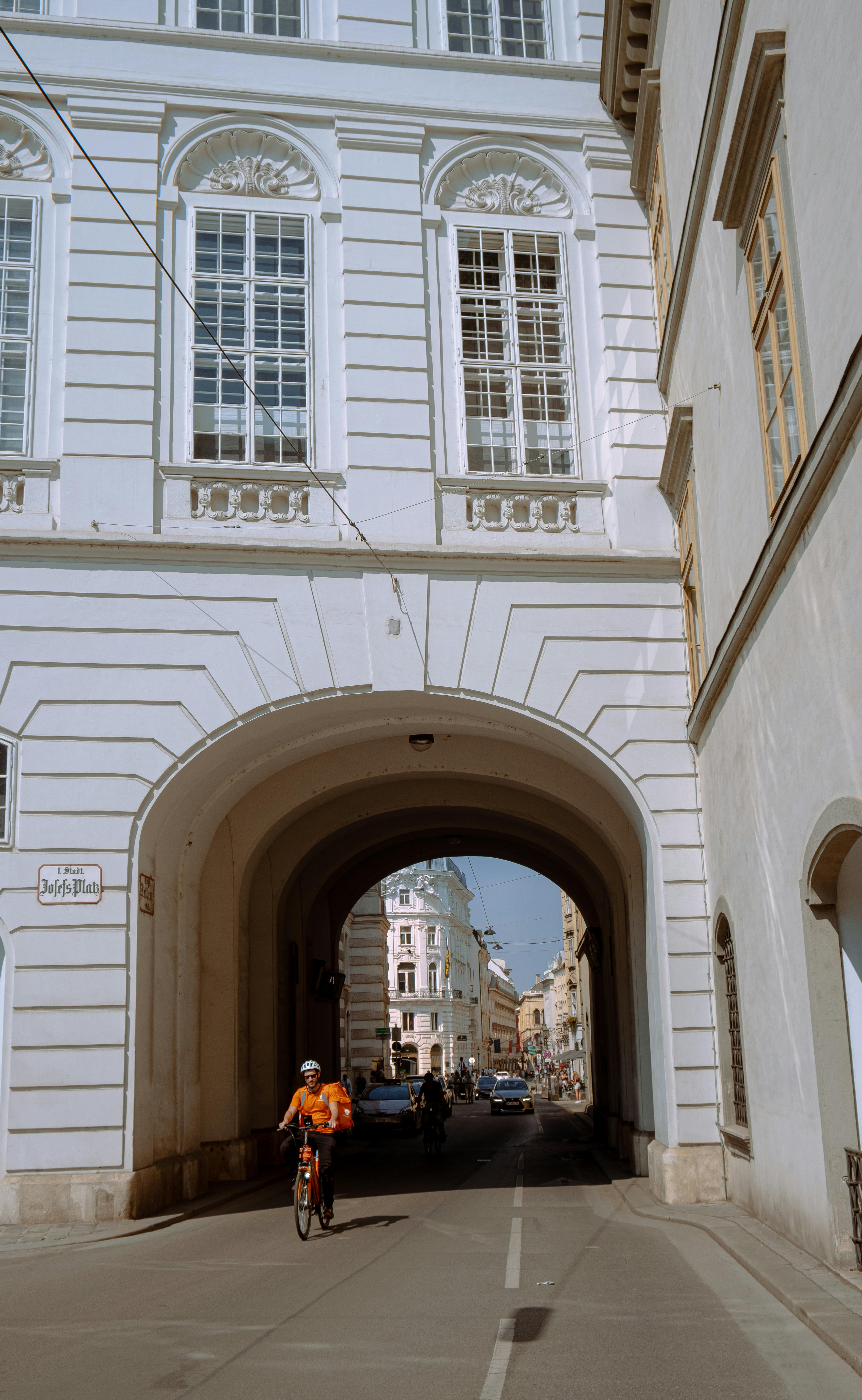 A cyclist rides through a historic archway on a sunny day in Vienna, Austria.