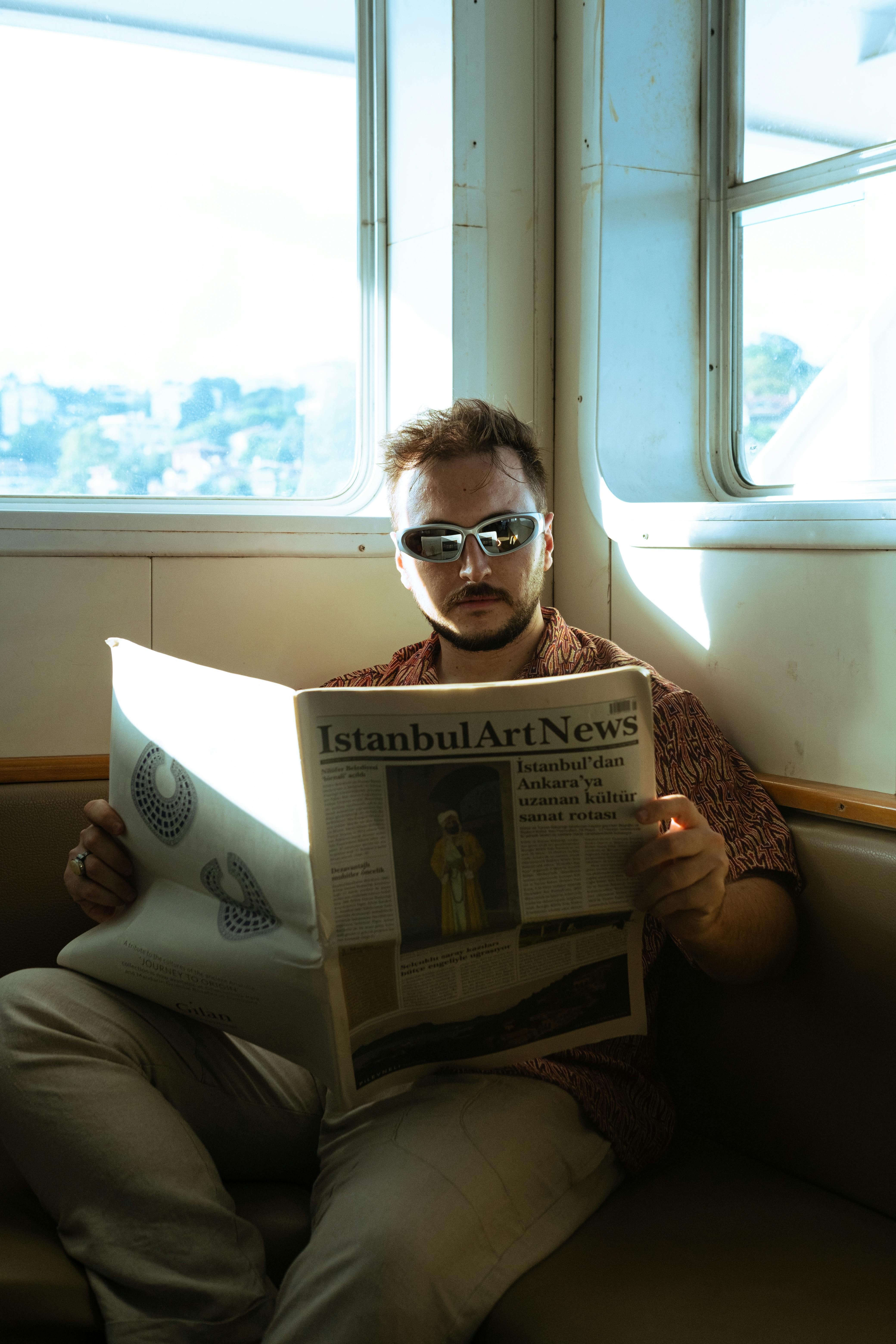 A man reads Istanbul Art News on a ferry with the city skyline in the background.