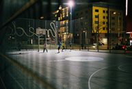 Men playing basketball on an urban court in Vienne at night.