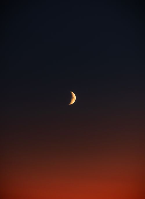 Free Crescent moon against a stunning twilight sky with gradient colors of orange and navy. Stock Photo