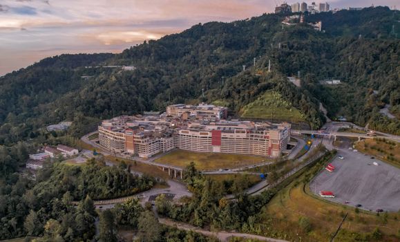 Drone captures a serene mountain resort surrounded by lush green hills at sunset.