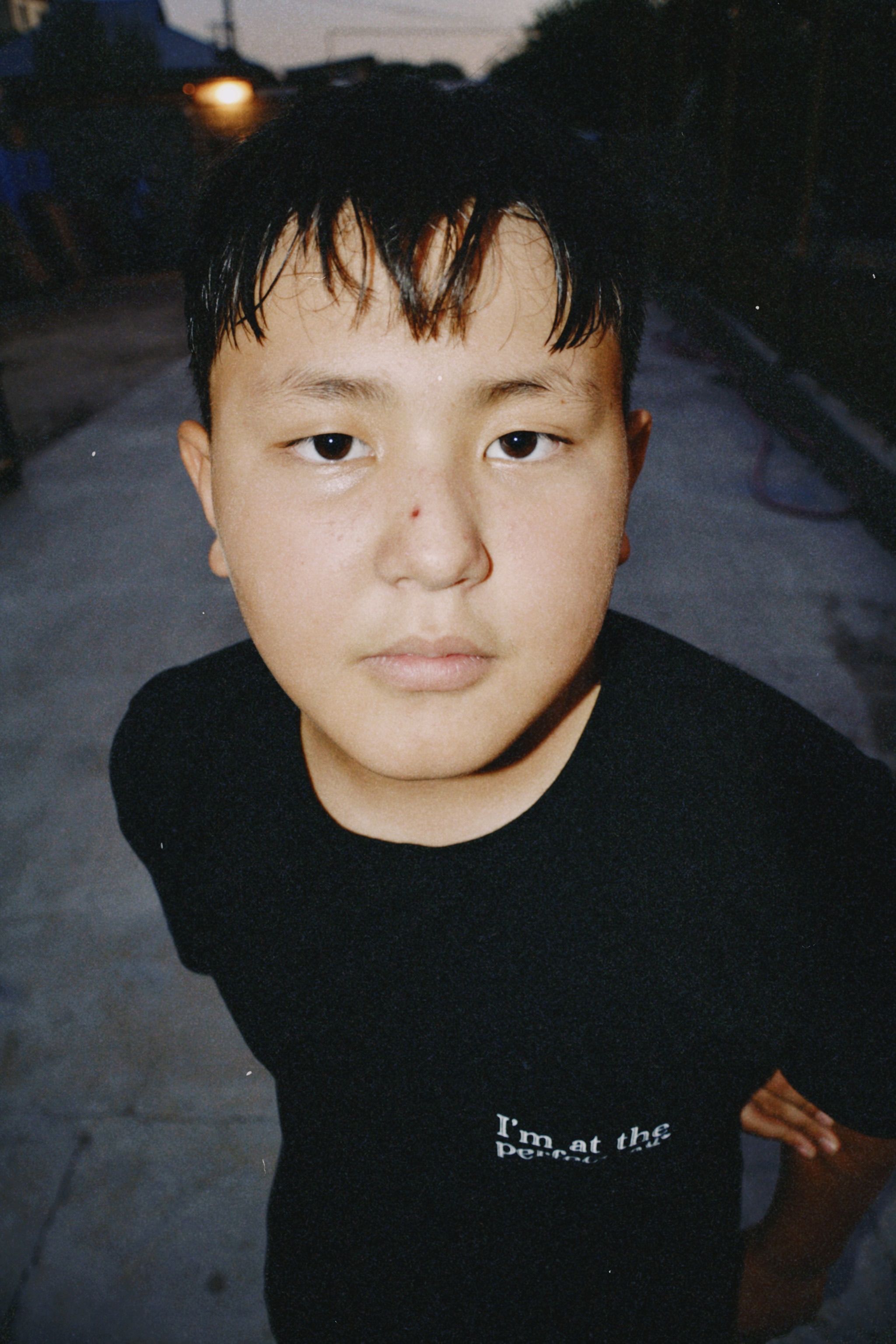Close-up portrait of a teenage boy on a city street in Shymkent during twilight, showcasing an urban atmosphere.