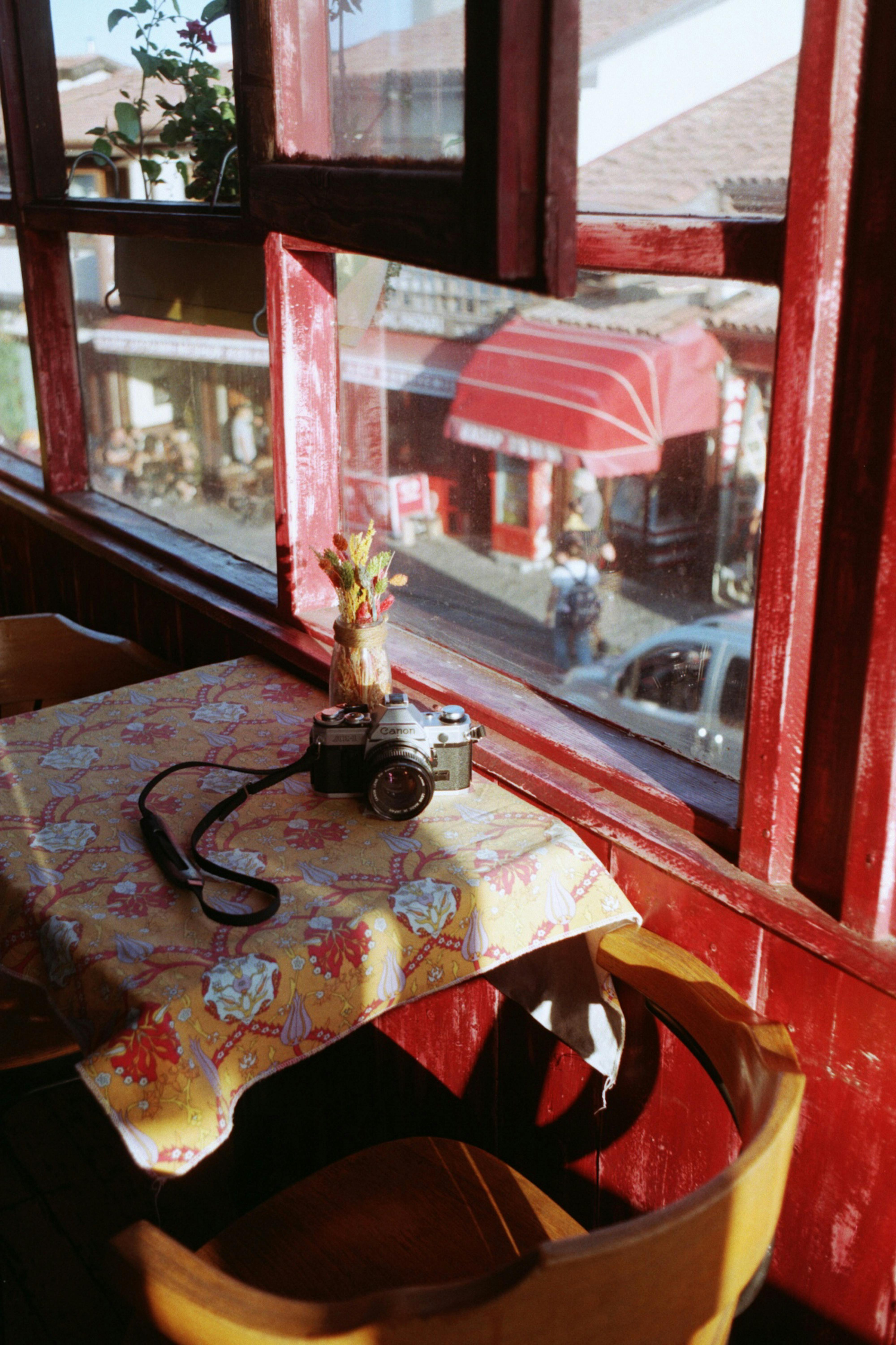 A vintage camera on a table by a window in a charming urban cafe setting.