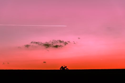 A motorcycle silhouette on the horizon with a stunning pink and orange sunset sky in the background.