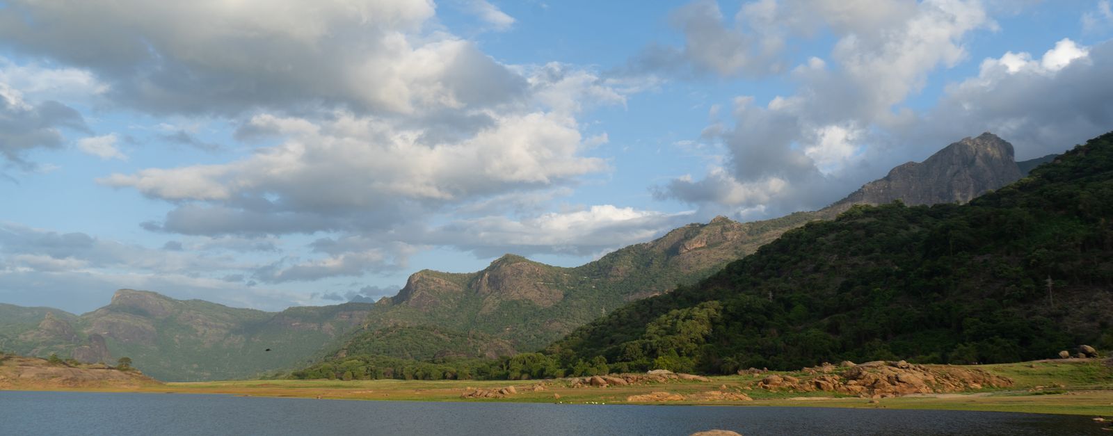 Beautiful landscape of Pollachi, TN, India featuring hills, a serene lake, and lush greenery under a blue sky