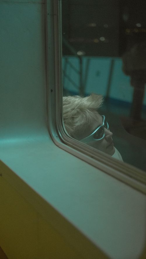 Free A woman with sunglasses gazes out a ferry window at night, reflecting solitude. Stock Photo