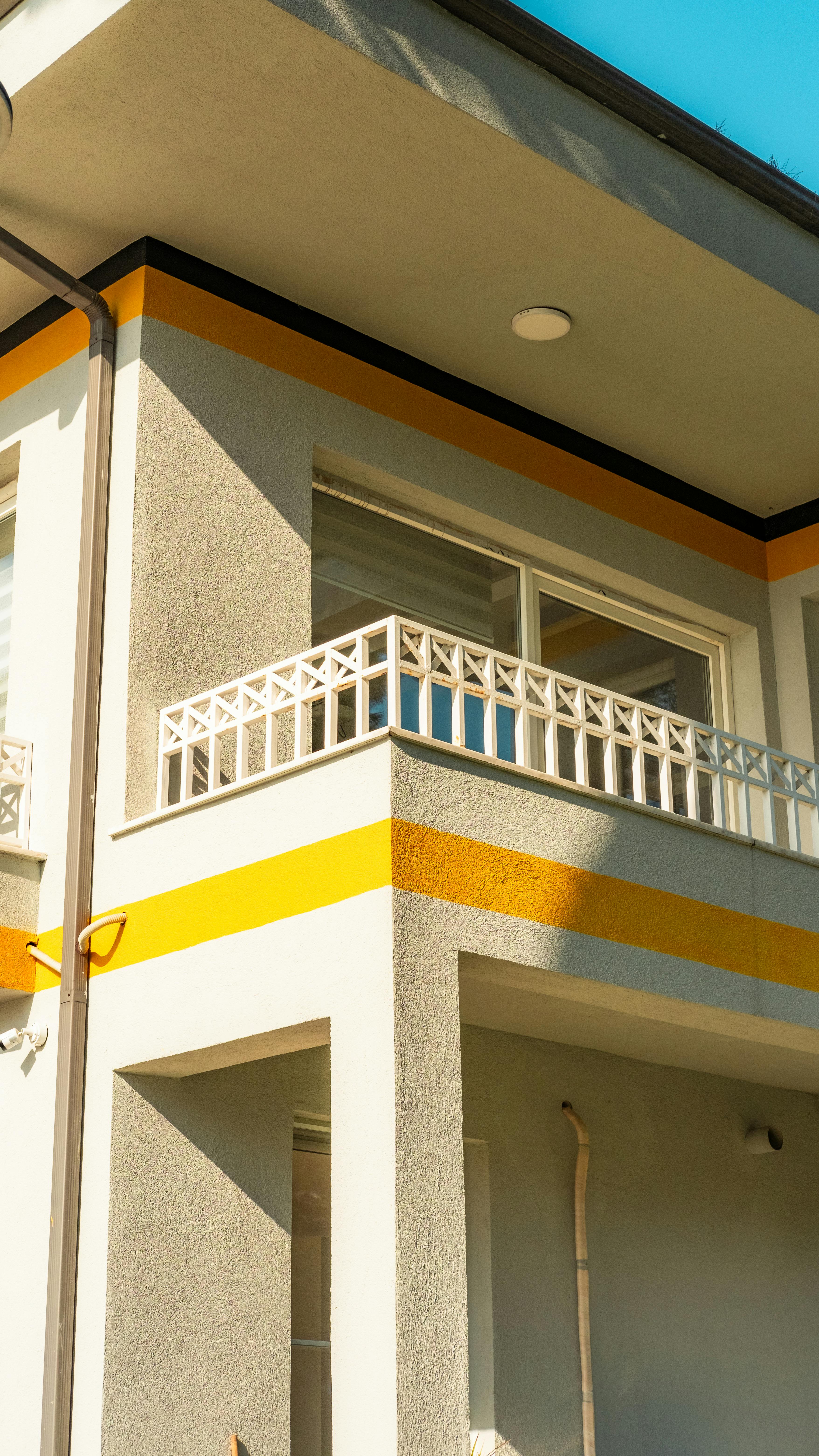 A modern residential building with a sunlit balcony, featuring geometric railings and bold color accents.