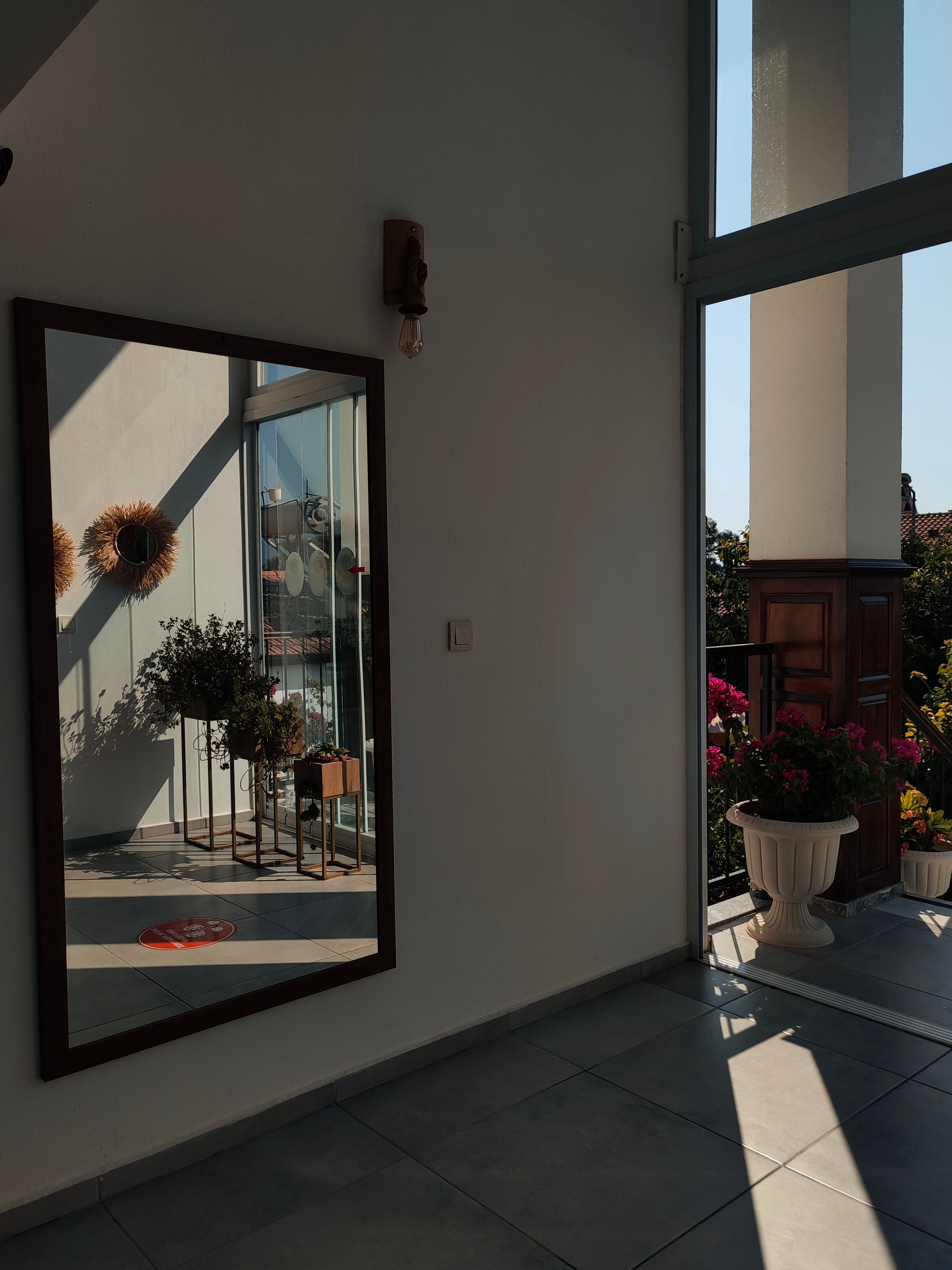 Mirror hung on a balcony wall reflecting light and greenery