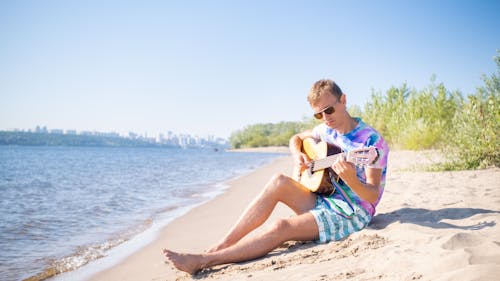 Young Man Sitting on Sand Beach Playing on Guitar