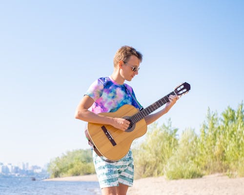 Young Man in Tie Dye T-Shirt Playing Acoustic Guitar on a Beach