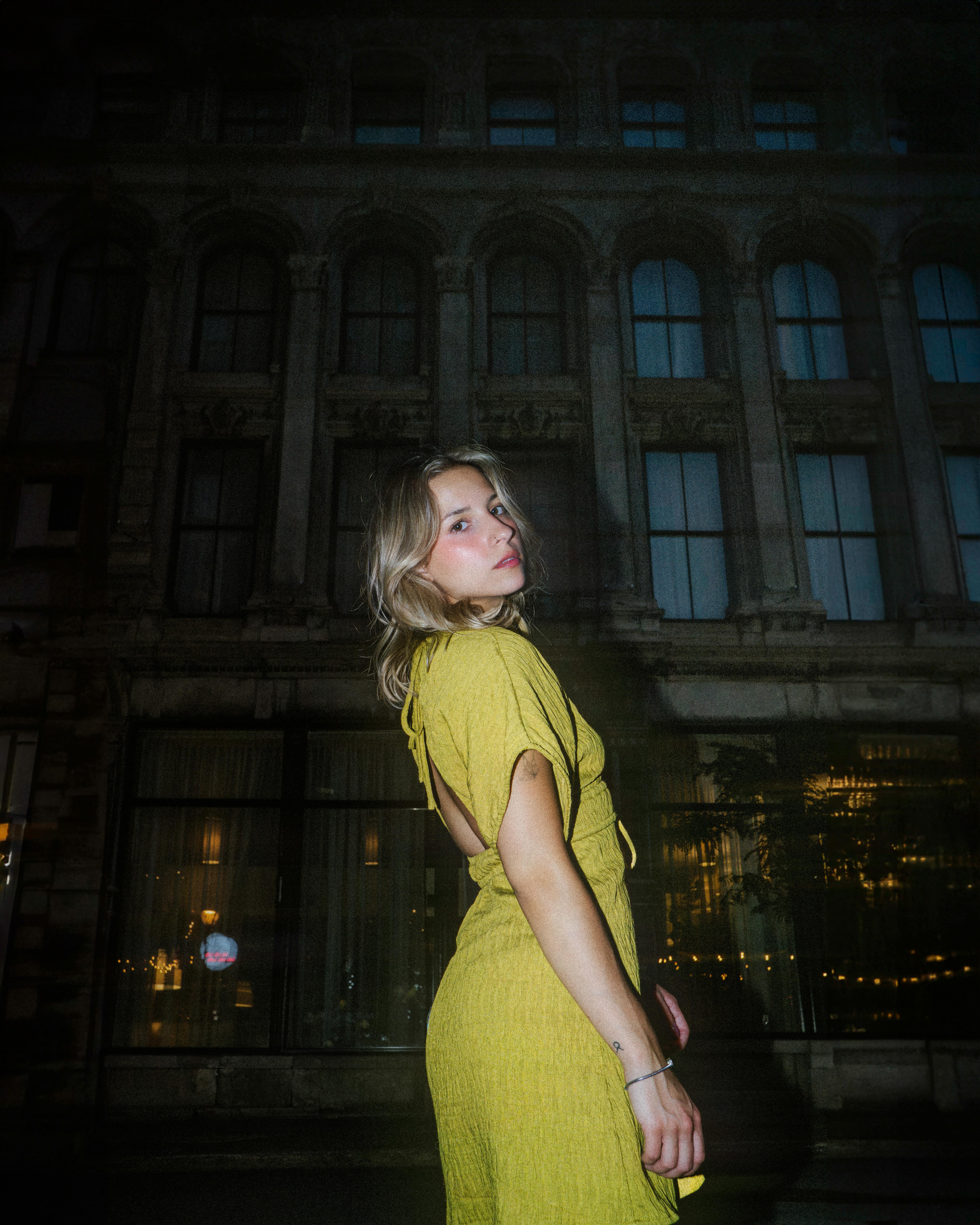 A stylish woman poses in a yellow dress in front of a historic building in Montreal at night.