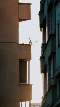 Silhouette of a city building's balcony with a satellite dish during sunset.