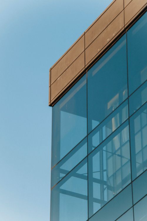 Free Sleek corner view of a modern glass building exterior against a clear blue sky. Stock Photo