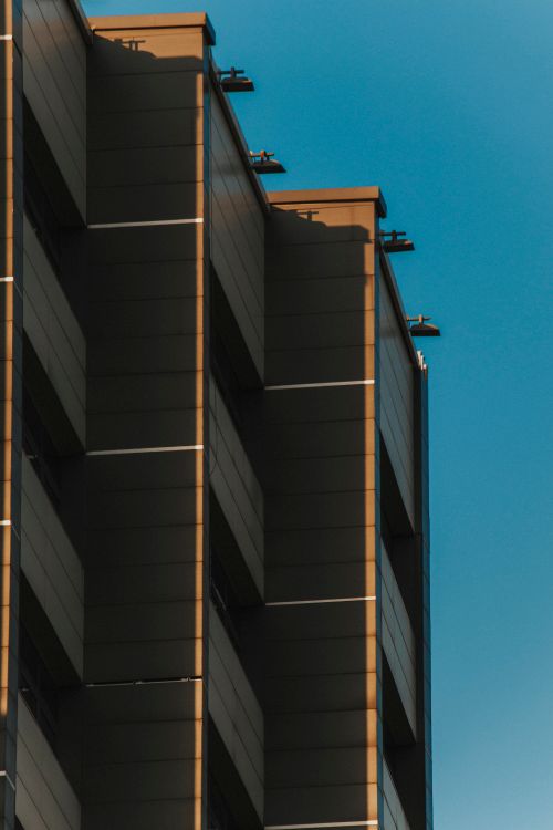Free Geometric facade of modern building casting shadows under clear blue sky. Stock Photo