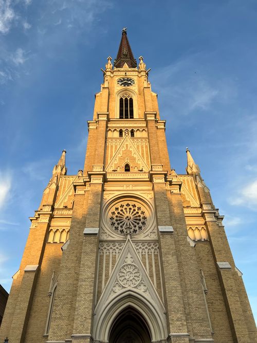 Free Capture of a Gothic church tower in Novi Sad, Serbia, lit by warm sunlight against a blue sky. Stock Photo