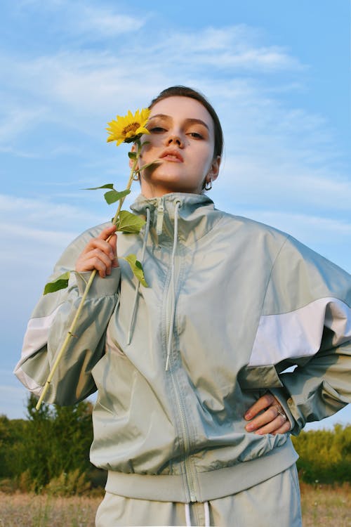 Free Woman in Nylon Tracksuit Holding a Sunflower in a Meadow Stock Photo