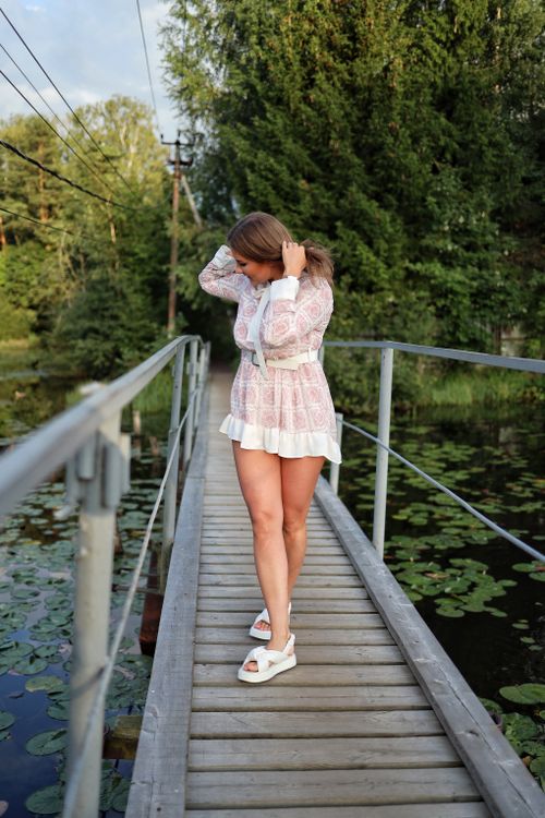 Free A woman in a dress walks on a wooden footbridge surrounded by lush greenery in a summer park. Stock Photo