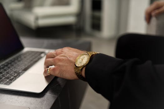 Close-up shot of a man's hand with a watch using a laptop touchpad indoors.